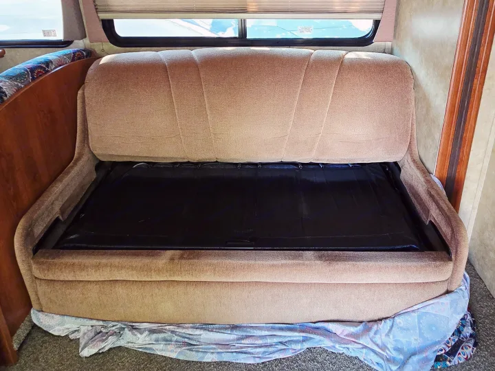 This RV rental features a tan convertible sofa with its backrest folded down, revealing the bed mechanism. RV interior.. Coachmen Freedom Express 2008