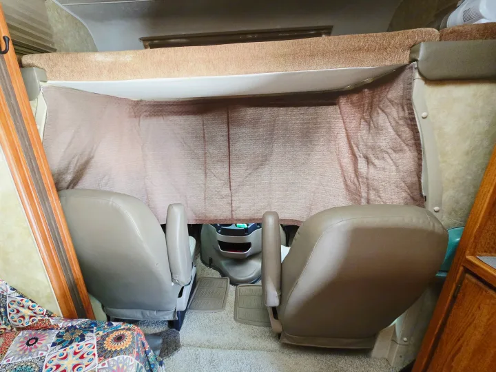 RV rental interior: Front cab with tan captain's chairs, an overhead bunk, and a beige privacy curtain drawn.. Coachmen Freedom Express 2008