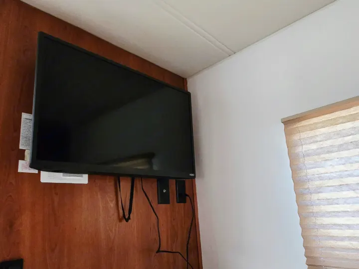 RV rental: Vizio television mounted on a wooden wall, with power cables and a pleated window blind in a compact space.. Coachmen Freedom Express 2008