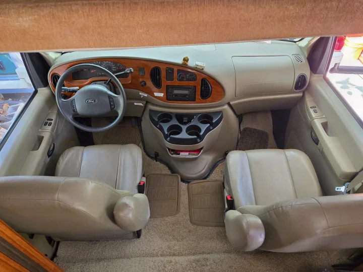 View of an rv rental's spacious front cabin with a Ford dashboard, tan seats, and center console, ready for adventure.. Coachmen Freedom Express 2008