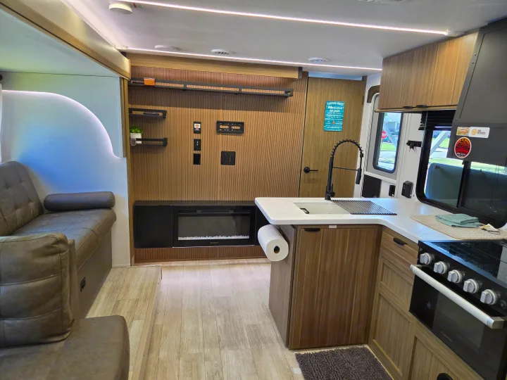 Inside a stylish RV rental: view of the kitchen with sink, Furrion stove, and living area featuring a sofa and electric fireplace.. Forest River Wildwood X-Lite 2025