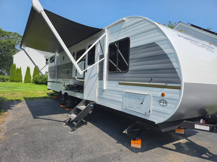 This Forest River Wildwood X-Lite rv rental is a travel trailer, parked with an extended awning, steps, and leveling blocks.. Forest River Wildwood X-Lite 2025