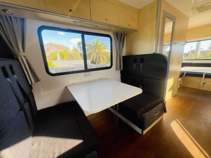 Bright RV rental dinette featuring dark seats, a white table, and large window views with sunlit trees outside.. Mercedes-Benz Other 2018