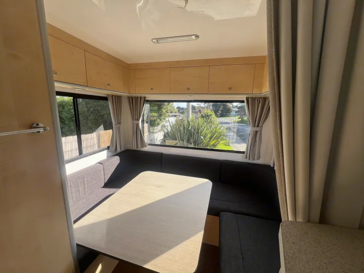 Bright RV rental dining area: U-shaped seating, light wood table & overhead cabinets, large windows offering scenic views.. Mercedes-Benz Other 2018