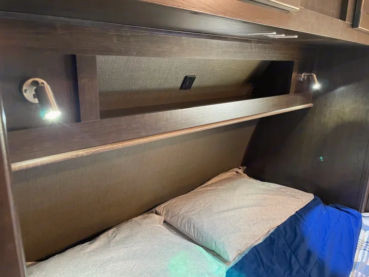 Cozy RV rental sleeping area showing bed with pillows, reading lights, and a convenient USB charging port in the overhead cubby.. Cruiser RV Shadow Cruiser 2019