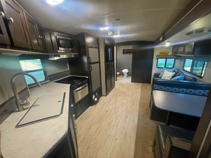 Clean rv rental interior shows kitchen with sink, stove, microwave, fridge, dining booth, and a glimpse of the bathroom.. Cruiser RV Shadow Cruiser 2019