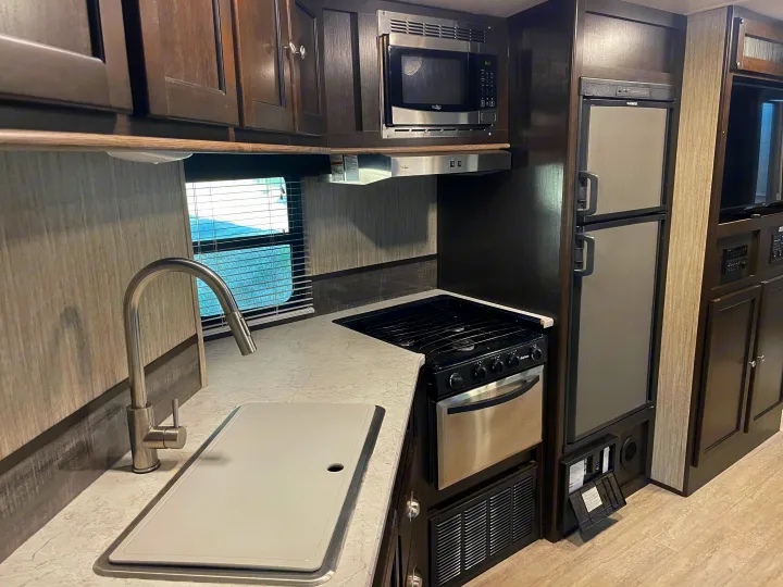 Modern RV rental kitchen featuring a microwave, stove, refrigerator, and sink. Fully equipped for your travels.. Cruiser RV Shadow Cruiser 2019