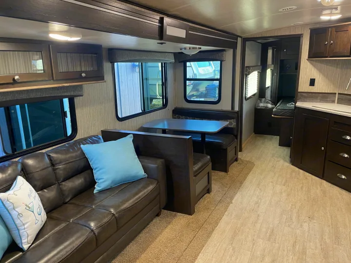 RV rental interior: Living area with dark leather couch, dining booth, kitchen, overhead cabinets, and light flooring.. Cruiser RV Shadow Cruiser 2019