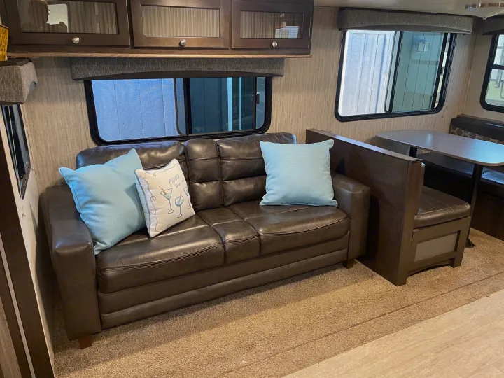 Cozy RV rental interior with a dark leather sofa, light blue pillows, and a dinette, offering a comfortable living space for your travel adventures.. Cruiser RV Shadow Cruiser 2019