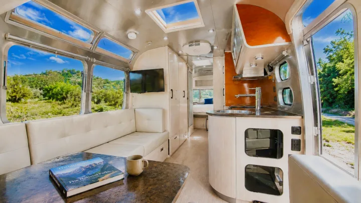 Modern Airstream rv rental interior: cream lounge, kitchen, bed, large windows with lush green landscape views.. Airstream International 2013