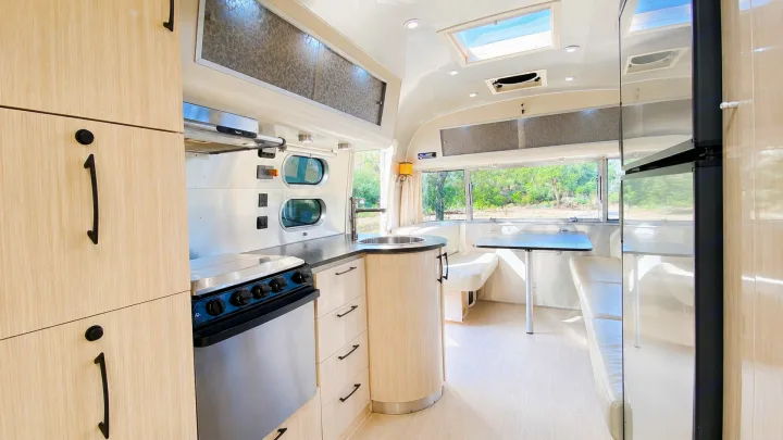 Bright RV rental interior: modern kitchen with light wood cabinets, stainless steel appliances, and a dinette by scenic windows.. Airstream International 2013