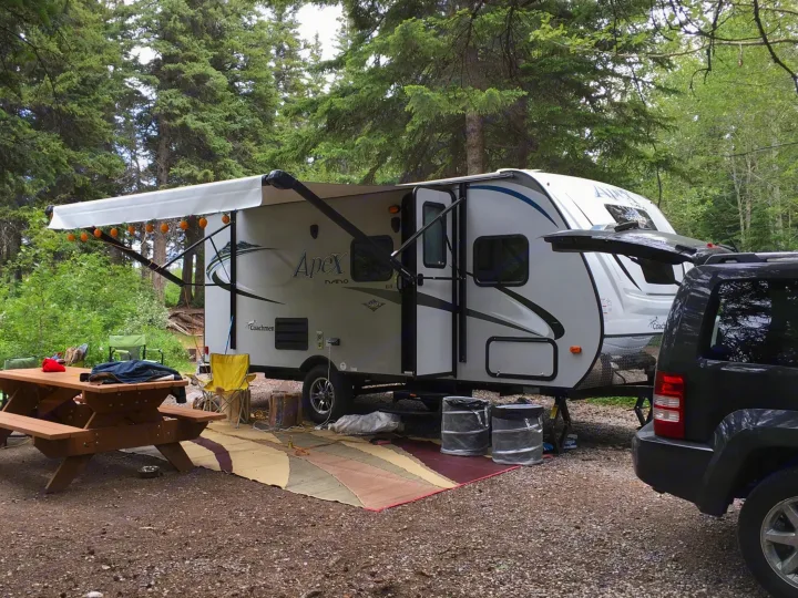 RV rental parked at a wooded campsite. An extended awning, picnic table, and SUV complete this outdoor setup.. Coachmen Apex Nano 2018