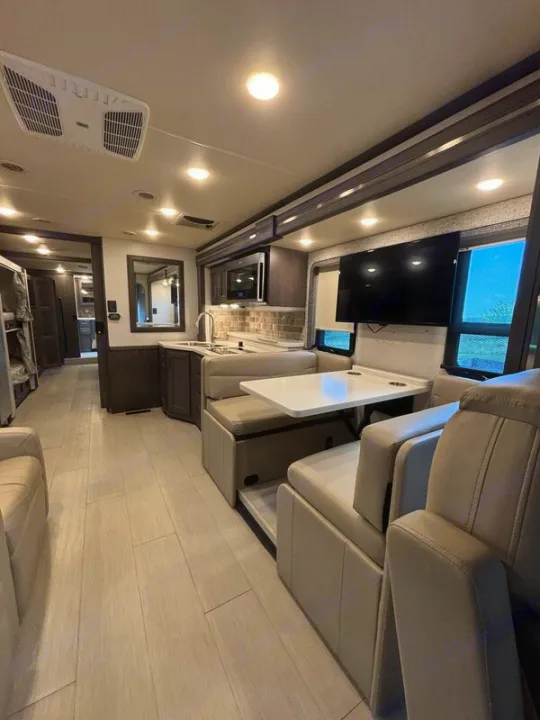 Modern rv rental interior: light-filled living area with kitchenette, dining booth, and comfortable seating for your travels.. Thor Palazzo 2023