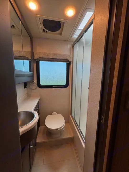 RV rental bathroom featuring a sink, vanity, toilet, and shower with sliding door. Well-lit and compact for travel comfort.. Thor Palazzo 2023