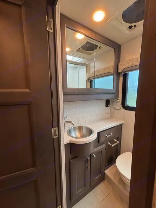 Inside an RV rental, a modern, compact bathroom featuring a vanity with a circular sink, mirrored cabinet, and toilet.. Thor Palazzo 2023