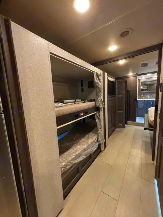 View inside an RV rental showing modern bunk beds, a compact sleeping area, and a hallway leading to the kitchen.. Thor Palazzo 2023