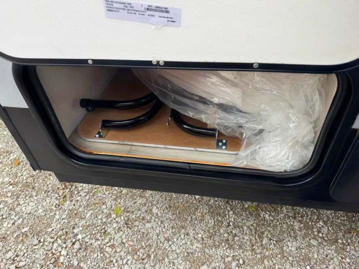 RV rental's open exterior storage shows a neatly packed folding table and plastic-wrapped mattress on a laminate floor.. Forest River Coachmen Clipper 2023