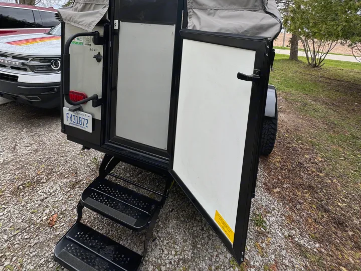 This **RV rental** offers adventure! Small camper with open door & steps on gravel, beside a Ford Bronco. Ready for camping.. Forest River Coachmen Clipper 2023