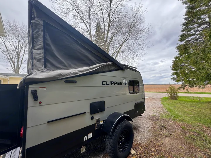 This Clipper pop-up travel trailer, ideal for rv rental, is set up outdoors with its pop-top extended for camping.. Forest River Coachmen Clipper 2023