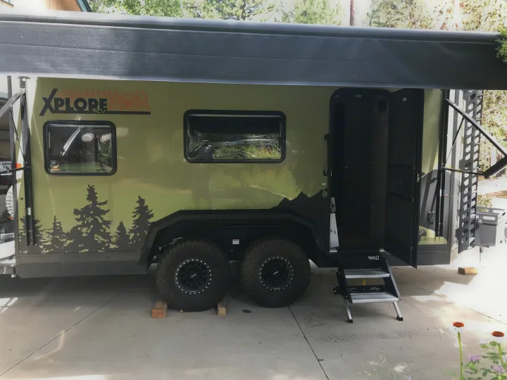 XPLORE off-road RV rental: a rugged olive-green travel trailer with an open awning, mountain graphics, and Solid Step entrance.. Imperial Outdoors XploreRV 2022