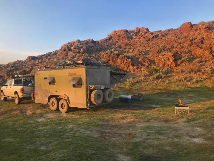 RV rental adventure: truck & XPLORE expedition trailer camp in rocky desert at dawn/dusk, with campfire.. Imperial Outdoors XploreRV 2022