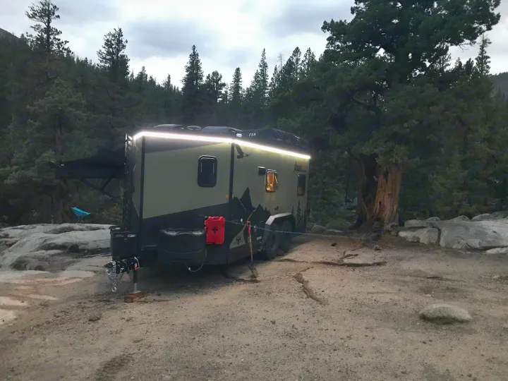 Off-road camper trailer (RV rental) lit at dusk in a forest camp with rocks & trees. Perfect for adventure camping.. Imperial Outdoors XploreRV 2022