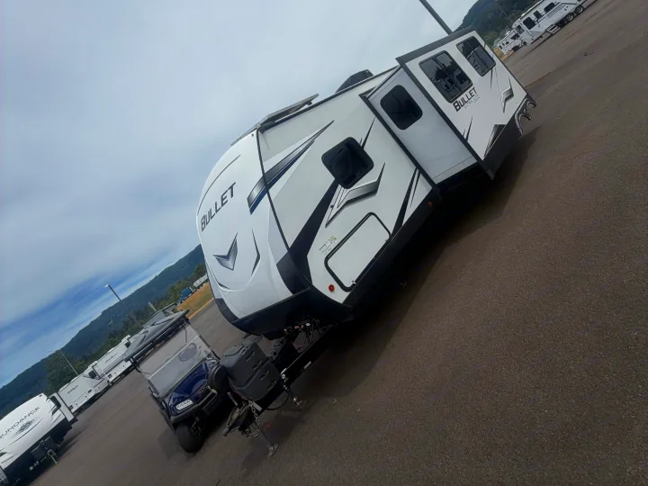 White Bullet travel trailer (RV) in a lot with a golf cart. Perfect for outdoor leisure and your next RV rental adventure.. Keystone RV Bullet Ultra Lite 2022