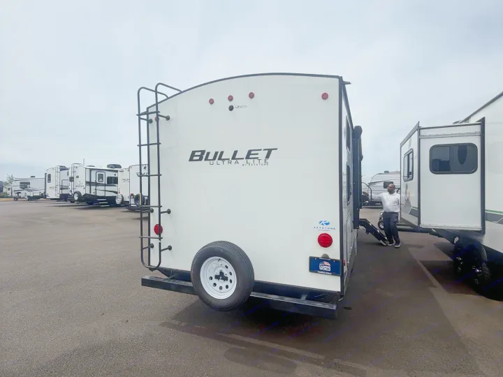 Rear of a white Keystone Bullet travel trailer at an RV rental lot. Other RVs are parked, with a person nearby.. Keystone RV Bullet Ultra Lite 2022