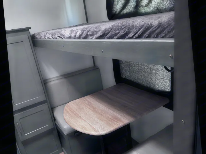 Cozy RV rental interior with a bunk bed over a dinette, featuring a light wood table and gray cabinet.. Keystone RV Bullet Ultra Lite 2022