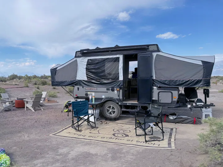 Rockwood pop-up camper RV rental at a scenic campsite with outdoor chairs, rug, and fire pit ready for adventure.. Forest River Rockwood ESP 2022