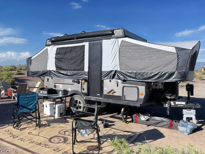 This Rockwood pop-up camper RV rental is set up for outdoor camping, complete with chairs, a table with a grill, and a cooler.. Forest River Rockwood ESP 2022