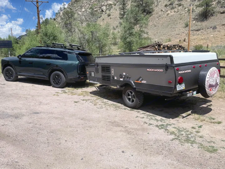 Dark green SUV towing a Rockwood ESP pop-up RV rental camper on a gravel road in a scenic, mountainous landscape.. Forest River Rockwood ESP 2022