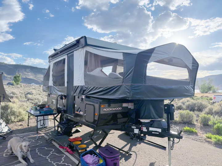 A Rockwood pop-up rv rental is set up for camping by a lake, with a yellow lab relaxing on an outdoor rug.. Forest River Rockwood ESP 2022