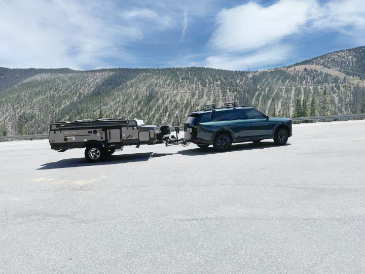 Dark green SUV towing a pop-up rv rental, parked against a backdrop of mountainous terrain and a partly cloudy sky.. Forest River Rockwood ESP 2022
