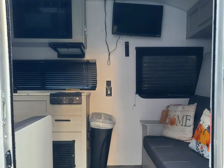 An rv rental's compact interior features a microwave, cooktop, Vizio TV, and sofa with seasonal pillows, seen from the doorway.. Forest River Salem FSX 2019
