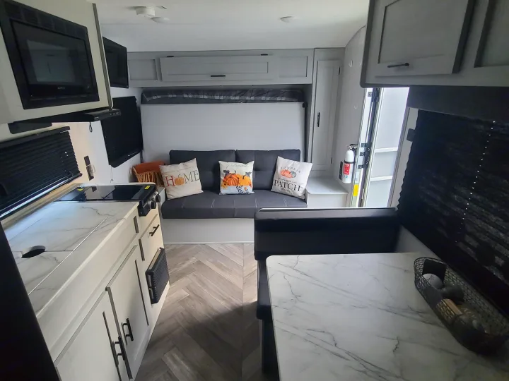 Bright and modern rv rental interior showcasing a kitchen, dining area, and sofa with fall-themed pillows.. Forest River Salem FSX 2019