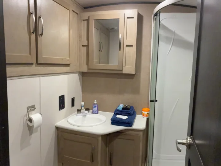 RV rental bathroom features a compact vanity, sink, mirror, toiletries, and curved shower stall for travelers.. Forest River Surveyor Luxury 2019