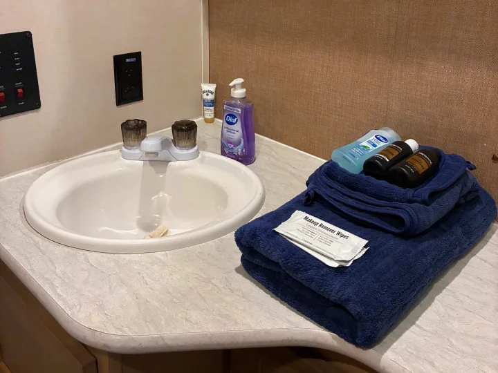 RV rental: Bathroom sink area featuring personal care items like soaps, creams, and fresh blue towels for guest comfort.. Forest River Surveyor Luxury 2019