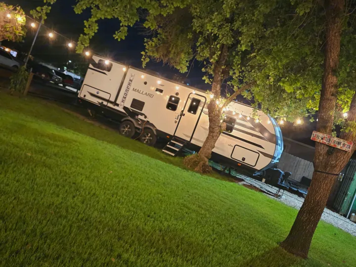 Nighttime RV rental at a cozy campsite with string lights and trees. Features a Mallard travel trailer.. Heartland RVs Mallard 2021