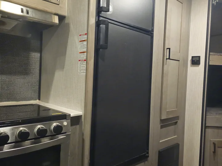 Modern RV rental interior with a kitchen area showing a stove, refrigerator, and contemporary cabinetry. Noticeable warning labels.. Heartland RVs Mallard 2021
