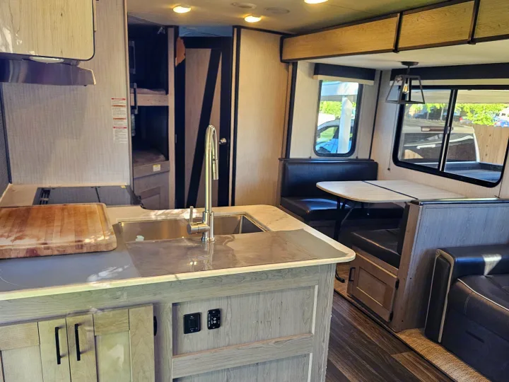 RV rental interior: kitchen island with sink & stovetop, dining booth, couch, and bunk beds visible in background.. Heartland RVs Mallard 2021