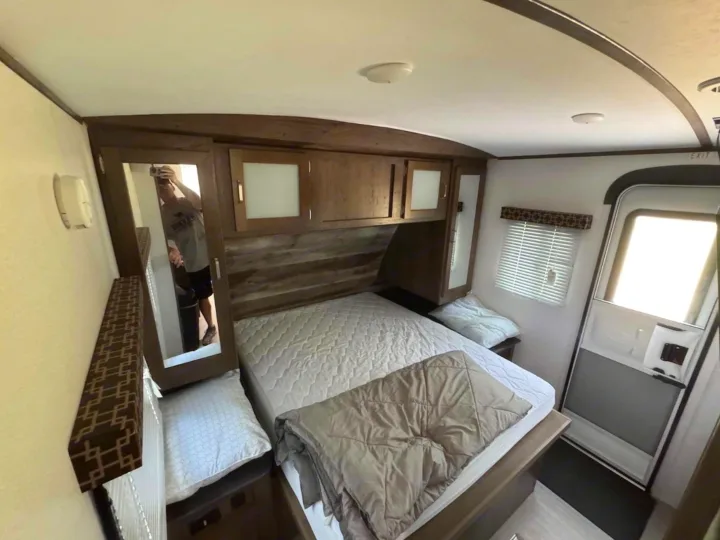 Explore this RV rental bedroom's interior: comfy bed, storage cabinets, and mirror. Ideal for your next camper trip.. Keystone RV Passport Grand Touring 2019