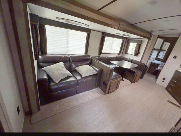 RV rental interior showcasing a spacious living area with a dark leather couch, U-shaped dinette, and large windows.. Keystone RV Passport Grand Touring 2019