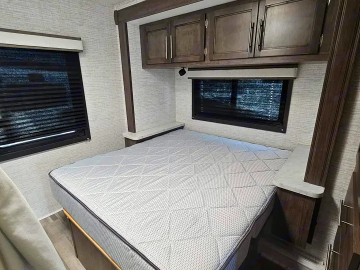 This RV rental features a comfortable bedroom setup with a light-patterned mattress, overhead storage, and window blinds.. Entegra Coach Odyssey SE 2025