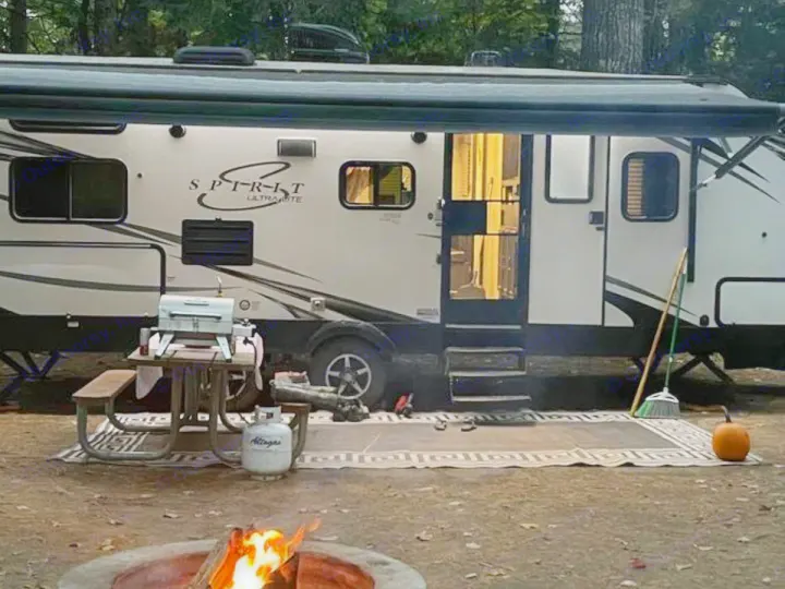 Experience an RV rental adventure! Cozy campsite with a travel trailer, crackling campfire, outdoor grill, and fall decor.. Coachmen Spirit 2019