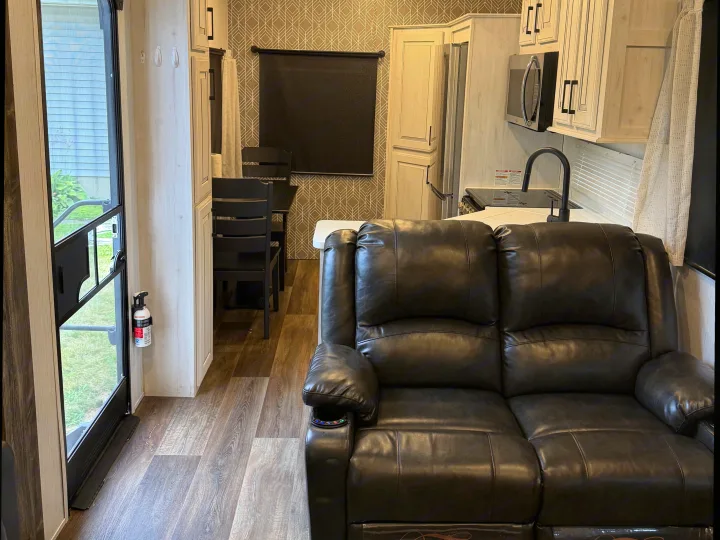 Modern RV rental living space featuring a cozy recliner sofa, full kitchen, and dining area. Perfect for travel comfort.. Heartland RVs Bighorn Traveler 2022