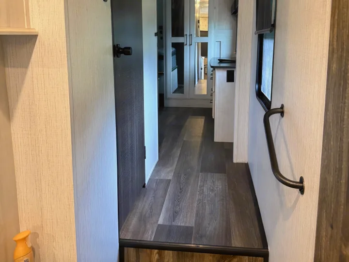 RV rental interior: A modern hallway with wood-look flooring, light textured walls, a dark door, and a grab bar for safety.. Heartland RVs Bighorn Traveler 2022