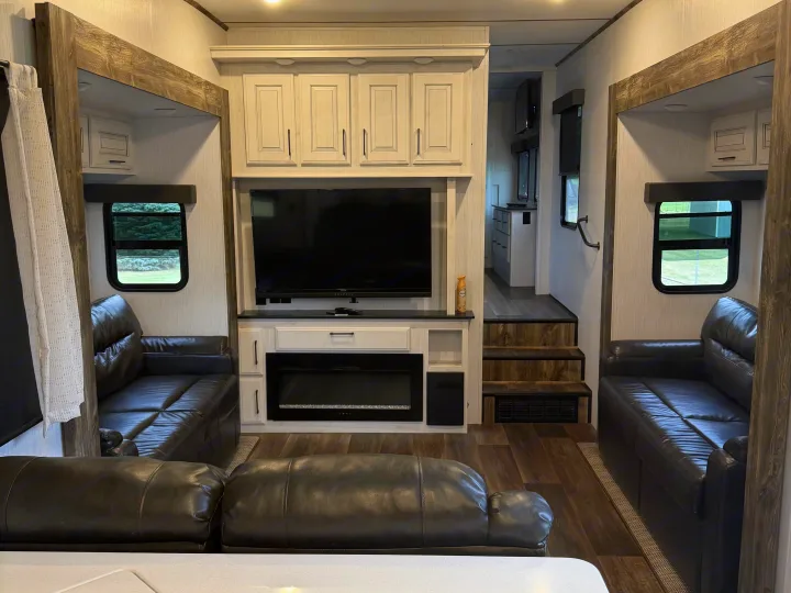 Spacious rv rental interior with a living area, two dark leather sofas, TV, fireplace, light cabinets, and wood-look floors.. Heartland RVs Bighorn Traveler 2022