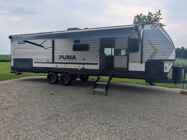 This PUMA travel trailer, with its awning out and steps down, is ready for your next rv rental adventure and camping trip.. Forest River 303BHCE Camping 2026