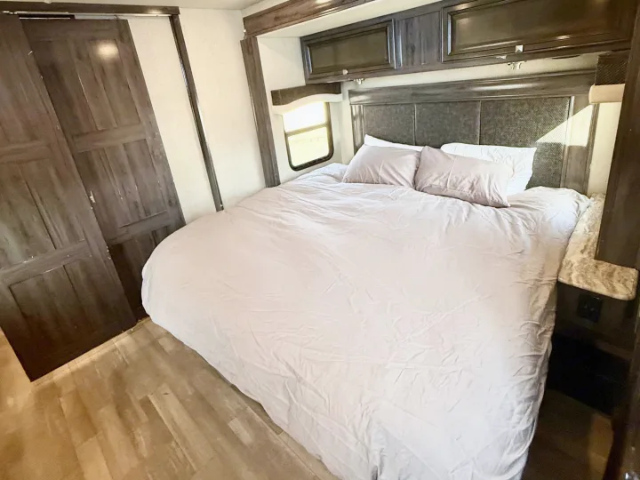 Cozy rv rental bedroom with a large bed, dark wood cabinets, a side window, and light wood flooring.. Flair-Fleetwood Flair-Fleetwood Motorhome 2020